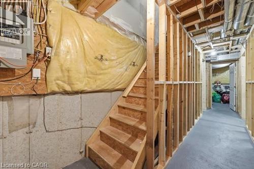 Unfinished basement space featuring exposed wood framing, concrete foundation walls, a wood staircase, and visible utility infrastructure including electrical paneling and ductwork - 16 Harrison Avenue, Hamilton, ON 
