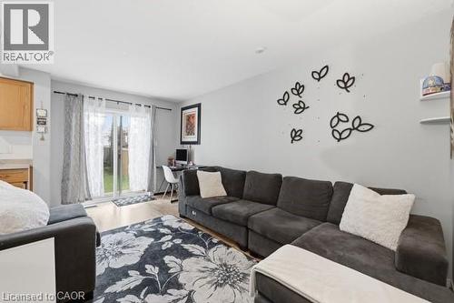 Light wood-finish flooring complements the neutral wall color in this versatile living area, featuring a sliding glass door providing direct outdoor access - 16 Harrison Avenue, Hamilton, ON 