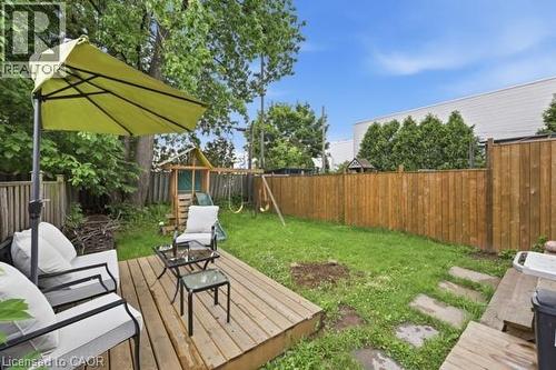 Expansive backyard featuring a wood deck patio, wooden privacy fencing, a patch of lawn, and mature trees - 16 Harrison Avenue, Hamilton, ON 