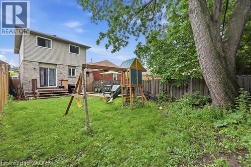 Expansive grassy backyard featuring a wooden privacy fence, mature trees, and a ground-level patio area - 16 Harrison Avenue, Hamilton, ON 