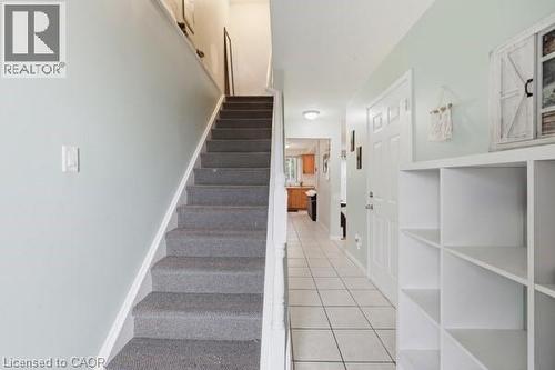Carpeted staircase with white risers and handrail, alongside a tiled entryway - 16 Harrison Avenue, Hamilton, ON 