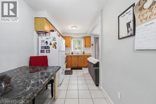 Kitchen featuring wood cabinetry, white tile flooring, and a window above the sink - 16 Harrison Avenue, Hamilton, ON 