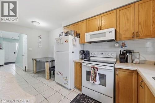 Kitchen featuring wood cabinetry, white appliances, subway tile backsplash, and tile flooring - 16 Harrison Avenue, Hamilton, ON 