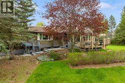 Front exterior featuring stone facade, wood decking, multiple trees, and a tiered stone pathway - 