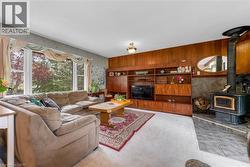 Living area with a built-in wood-finish entertainment center, a wood-burning stove with a stone surround, and large windows providing natural light - 