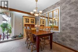Carpeted dining area featuring a decorative wall finish, an ornate chandelier, a built-in display cabinet with glass doors, and a mirrored wall accent - 