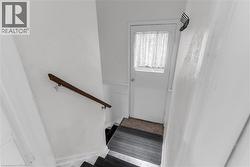 Stairwell featuring a wood handrail, white painted walls, and dark stair treads - 
