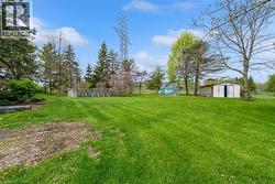 Expansive lawn featuring mature trees, an above-ground pool, and multiple outbuildings for storage - 