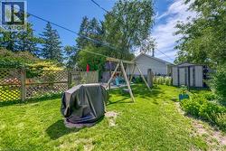 Expansive grassy backyard featuring a swing set, mature perimeter trees, a garden shed, and a lattice privacy fence - 