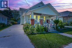 Charming residence featuring a welcoming front porch with brick pillars and wood railings, a well-maintained lawn, established landscaping, and a concrete driveway - 