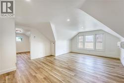 Spacious room featuring sloped ceilings, wood-finish flooring, recessed lighting, a trio of windows, and an interior wall unit - 