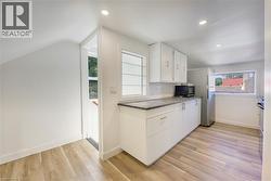 Contemporary kitchen featuring white cabinetry, dark speckled countertops, and wood-finish flooring - 