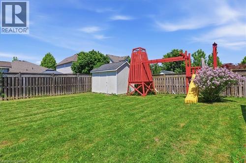 Expansive lawn area featuring a wooden picket fence, a detached storage shed, and a prominent red playset with a yellow slide - 43 Decaro Crescent, Cambridge, ON 