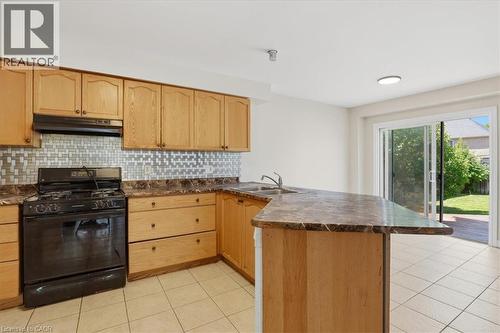 Kitchen featuring wood cabinetry, a mosaic tile backsplash, a black gas range, and a breakfast bar - 43 Decaro Crescent, Cambridge, ON 