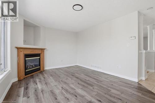 Corner fireplace with a light wood mantel, grey wood-finish flooring, white baseboards, and a circular ceiling light fixture - 43 Decaro Crescent, Cambridge, ON 