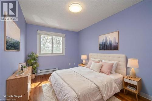 Bedroom featuring wood-finish flooring, a white trim window, a baseboard heater, a ceiling light fixture, and light-colored walls - 121 Morgan Avenue Unit# 7, Kitchener, ON 