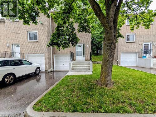 Brick facade townhouse featuring a ground-level garage, concrete steps, and a front entrance with a storm door - 121 Morgan Avenue Unit# 7, Kitchener, ON 
