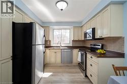 Kitchen featuring cream-colored cabinetry, stainless steel appliances, a window above the sink, wood-finish flooring, and a tiled backsplash - 