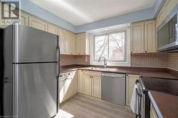 Kitchen featuring light-toned cabinetry, stainless steel appliances, a tile backsplash, and wood-finish flooring - 