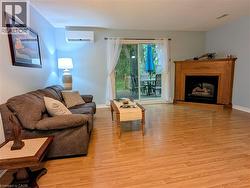 Living area featuring light wood-finish flooring, a corner-mounted fireplace with a wooden mantel, and a sliding glass door providing access to an outdoor patio - 