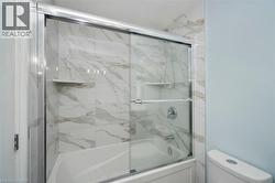 Tub-shower combination featuring a sliding glass enclosure, white and gray veined tile surround, and an integrated shower niche - 