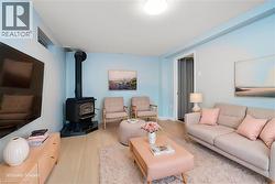 Living area featuring a black wood-burning stove on a dark tile hearth, pale blue walls, light wood-finish flooring, and a recessed window - 
