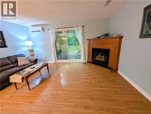 Spacious room featuring wood-finish flooring, a corner fireplace with a wooden mantel, and a wall-mounted mini-split unit - 121 Morgan Avenue Unit# 7, Kitchener, ON 