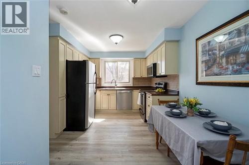 Bright kitchen featuring light-toned cabinetry, dark countertops, a tile backsplash, stainless steel appliances, and wood-finish flooring - 121 Morgan Avenue Unit# 7, Kitchener, ON 