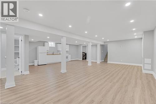 Spacious lower level featuring wood-finish flooring, recessed lighting, support columns, a kitchen area with white cabinetry and a wood-finish countertop, and a separate laundry area - 44 Mcclellan Road, Alton, ON 