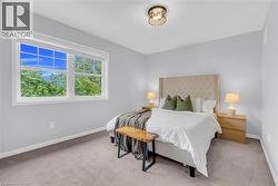 Bright bedroom featuring a large window with white trim, light gray walls, and neutral carpeting - 