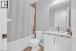 Bathroom featuring a white bathtub with a shower curtain, a toilet, and a vanity with a rectangular sink - 