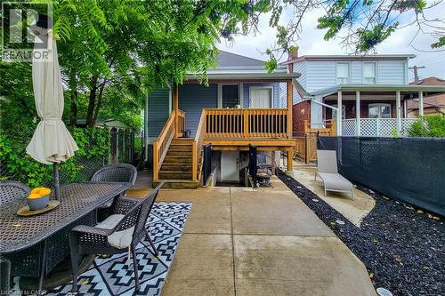 Backyard patio with concrete surfacing and a raised wood deck featuring a balustrade and stairs - 58 East 22Nd Street, Hamilton, ON 