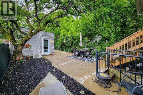 Concrete patio with a detached outbuilding featuring horizontal siding and a white entry door - 58 East 22Nd Street, Hamilton, ON 