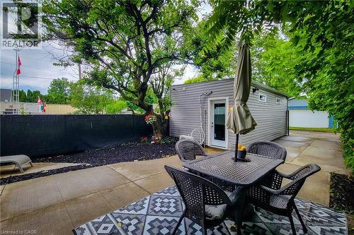 Concrete patio with a patterned outdoor rug, complemented by a detached outbuilding with gray siding and transom windows - 58 East 22Nd Street, Hamilton, ON 