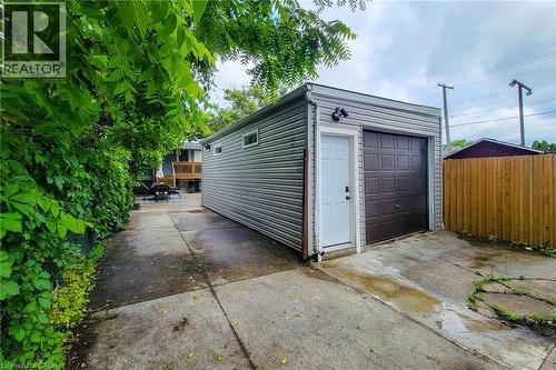 Detached garage with horizontal siding, a brown panel garage door, and a white access door - 58 East 22Nd Street, Hamilton, ON 