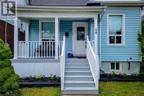Blue siding exterior with a white-railed porch featuring a white entry door, gray steps, and white window trim - 58 East 22Nd Street, Hamilton, ON 