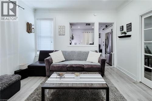 Spacious living area featuring light wood-finish flooring, white walls, and a large window with blinds - 58 East 22Nd Street, Hamilton, ON 