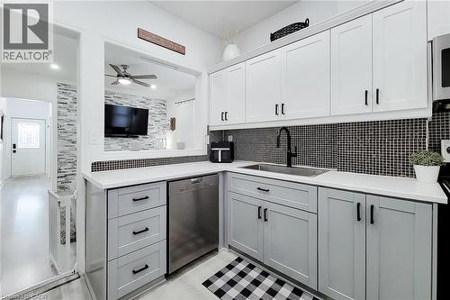 Kitchen featuring white upper cabinetry, grey lower cabinetry, stainless steel sink with matte black faucet, and a black and white mosaic tile backsplash - 58 East 22Nd Street, Hamilton, ON 