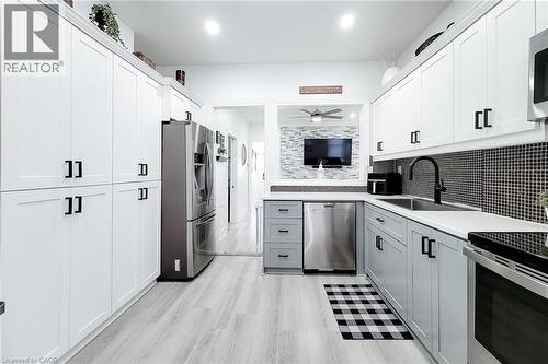 Modern kitchen featuring light wood-finish flooring, two-tone cabinetry with black hardware, stainless steel appliances, and a mosaic tile backsplash - 58 East 22Nd Street, Hamilton, ON 