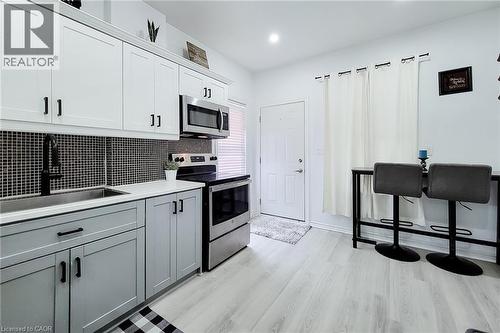 Kitchen featuring stainless steel appliances, mosaic tile backsplash, two-tone cabinetry, and wood-finish flooring - 58 East 22Nd Street, Hamilton, ON 