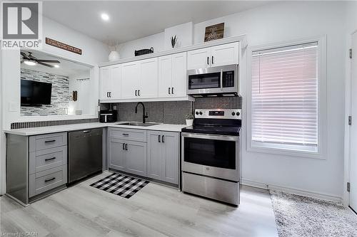 Kitchen featuring two-tone cabinetry with black hardware, stainless steel appliances, and wood-finish flooring - 58 East 22Nd Street, Hamilton, ON 