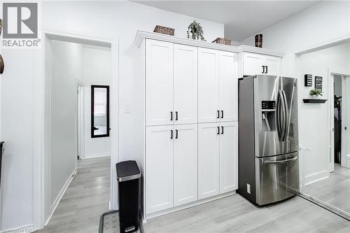 Full-height white cabinetry with black hardware, stainless steel refrigerator, light wood-finish flooring, white walls, and a mirrored closet door - 58 East 22Nd Street, Hamilton, ON 
