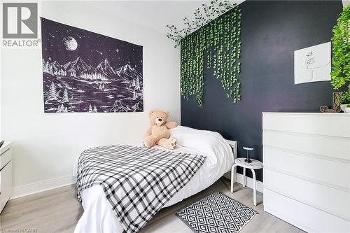 Bedroom featuring a dark accent wall with artificial hanging greenery, light wood-finish flooring, white baseboards, and white painted walls - 58 East 22Nd Street, Hamilton, ON 