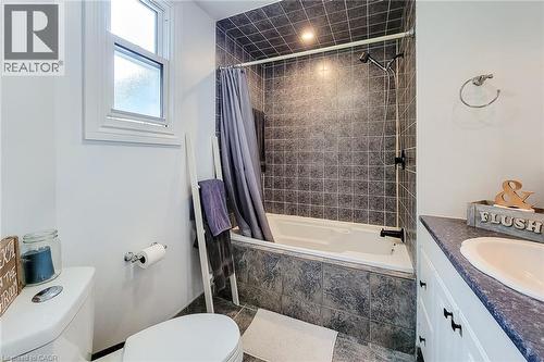 Bathroom featuring a tub/shower combination with tile surround, a white vanity with a built-in sink, and a single window - 58 East 22Nd Street, Hamilton, ON 