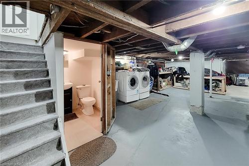 Basement utility space featuring a full staircase with carpeted treads, a dedicated laundry area with appliances, and a separate half-bathroom with a vanity sink and toilet - 58 East 22Nd Street, Hamilton, ON 