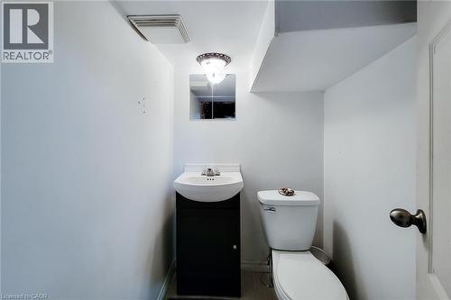 Compact powder room featuring a pedestal sink with dark wood-finish vanity, wall-mounted mirror, and overhead light fixture - 58 East 22Nd Street, Hamilton, ON 