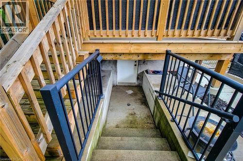 Lower-level concrete patio with a white entry door, framed by concrete retaining walls and black metal railings - 58 East 22Nd Street, Hamilton, ON 