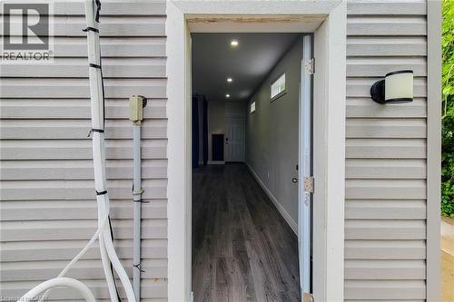 Siding exterior featuring a contemporary outdoor wall sconce and an open doorway revealing interior wood-finish flooring, recessed lighting, and transom windows - 58 East 22Nd Street, Hamilton, ON 