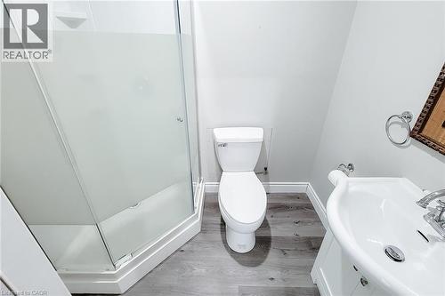 Compact bathroom featuring a corner shower with frosted glass enclosure, white toilet, and a pedestal sink with chrome fixtures - 58 East 22Nd Street, Hamilton, ON 