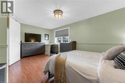 Bedroom featuring wood-finish flooring, a contemporary ceiling light fixture, a window with a roller shade, and light green walls with chair rail molding - 
